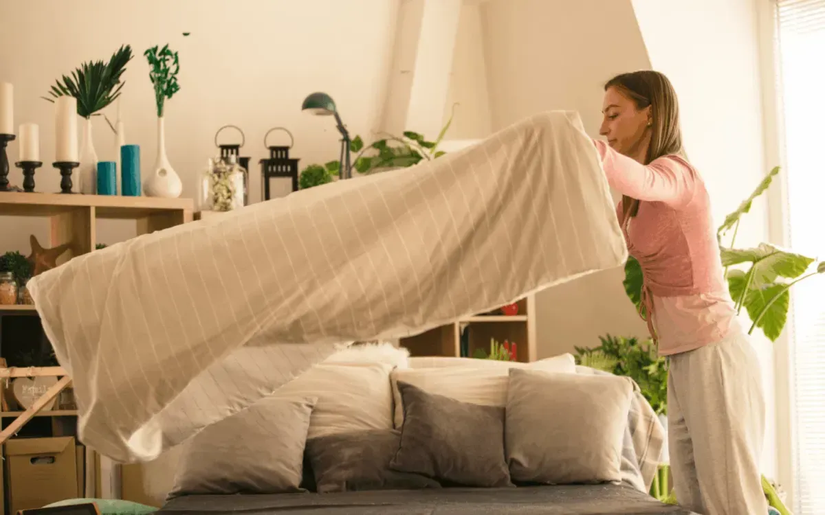 Woman making bed and changing linens during professional home cleaning service.